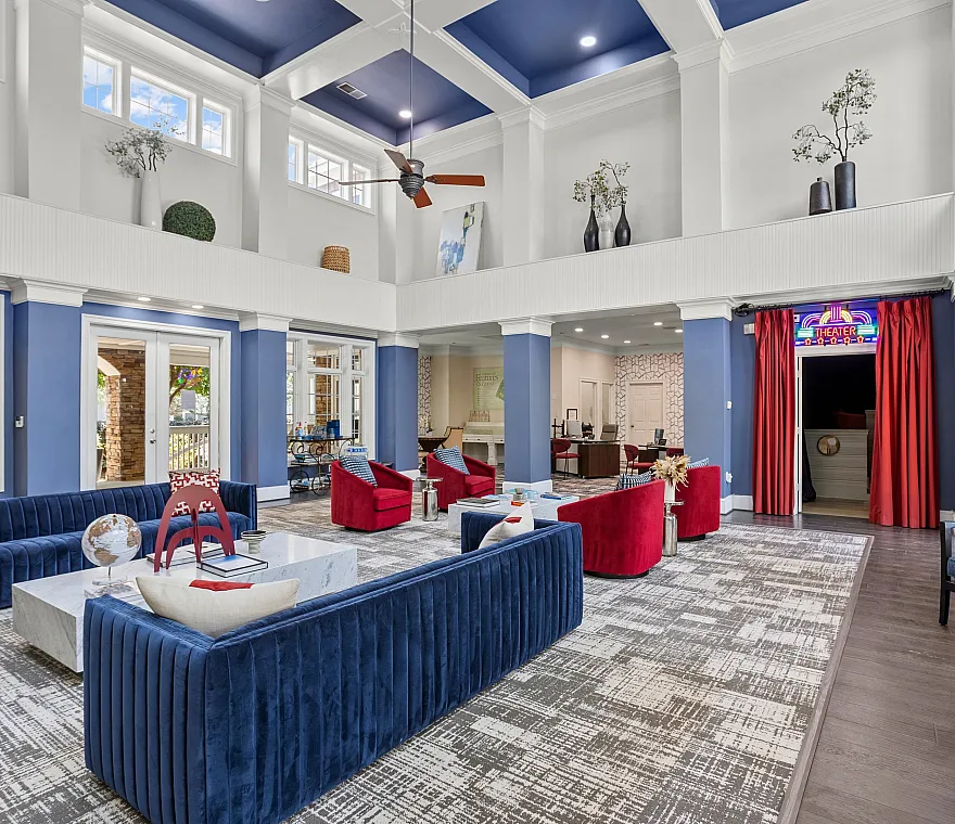 Luxurious residential lounge with high ceilings, elegant blue and red seating, a chic marble coffee table, and a stylish mini theater room entrance.