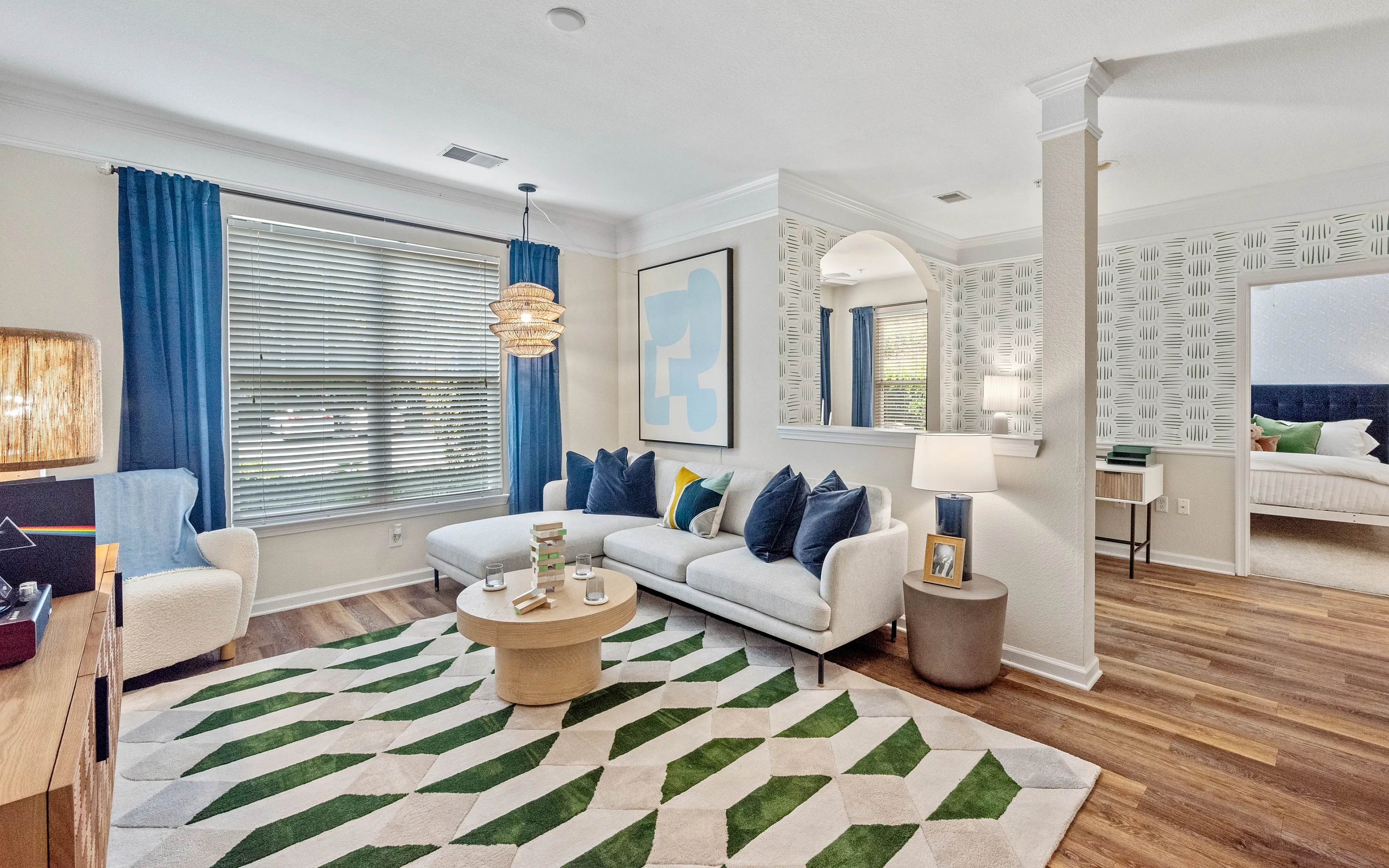 Chic living room with modern decor, featuring a cozy sectional sofa, stylish blue curtains, and a geometric-patterned rug. Elegant lighting and vibrant accents create a welcoming atmosphere, perfect for relaxation and entertaining.