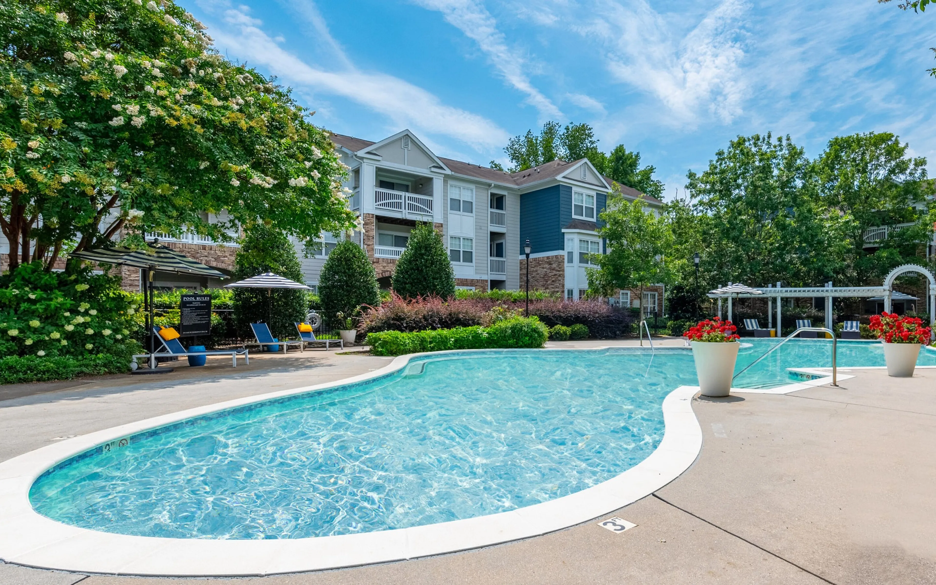 Inviting outdoor swimming pool surrounded by lush greenery and stylish apartment buildings, perfect for relaxation and leisure.