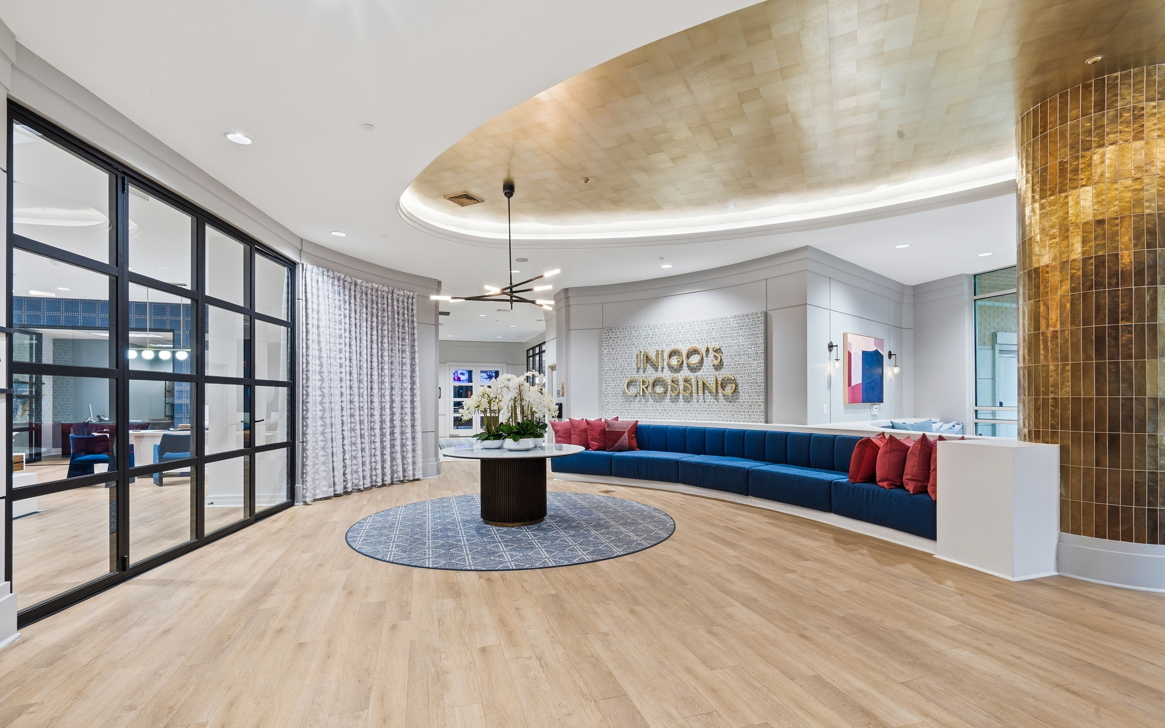 Elegant apartment lobby with modern decor, featuring a curved blue seating area, chic lighting, and a stylish circular table centerpiece.