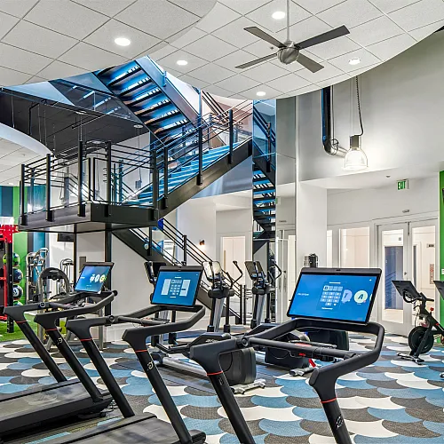Modern fitness center with state-of-the-art cardio equipment, vibrant design, and sleek spiral staircase.