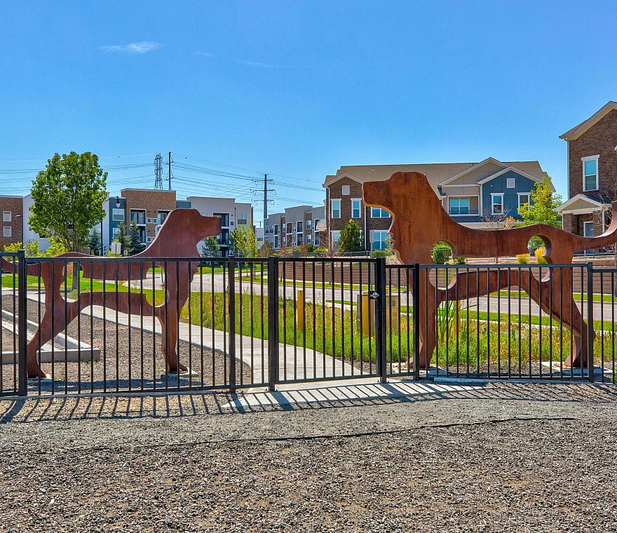 Charming gated residential community entrance featuring artistic dog silhouette designs, vibrant green surroundings, and modern architecture in the background.