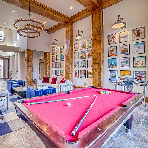 Elegant community lounge featuring a vibrant red pool table, cozy seating area with plush sofas, and a stunning gallery wall of art under warm ambient lighting.
