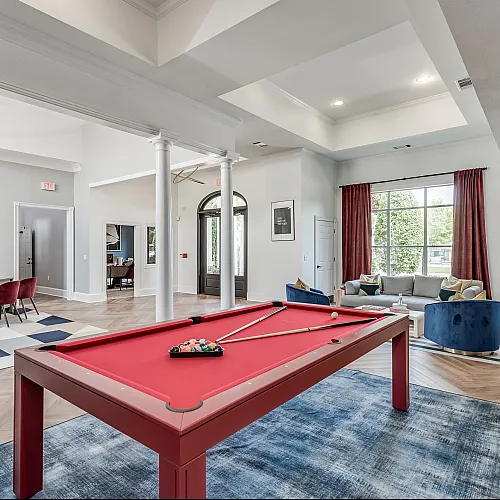 Luxurious community room with vibrant red pool table, elegant seating area, and modern decor, offering a bright, spacious ambiance.