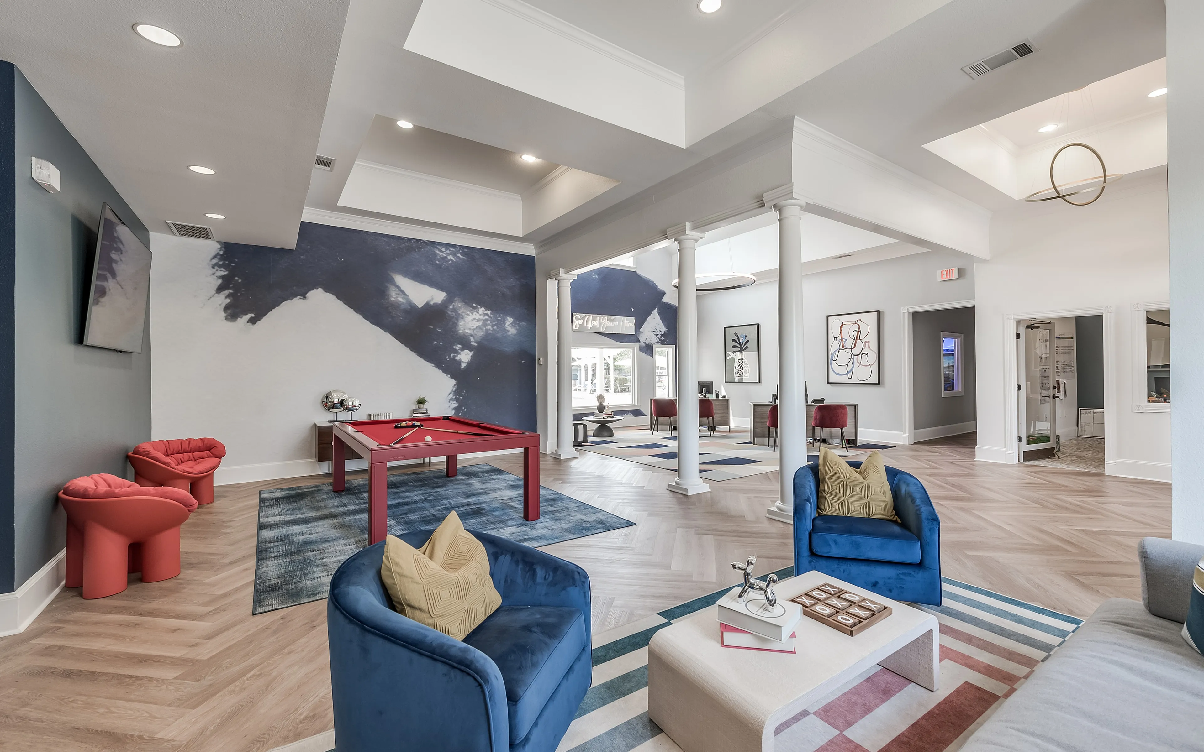 Modern recreational room with elegant blue-themed decor, featuring a stylish red pool table and cozy seating area under a high ceiling with contemporary lighting.