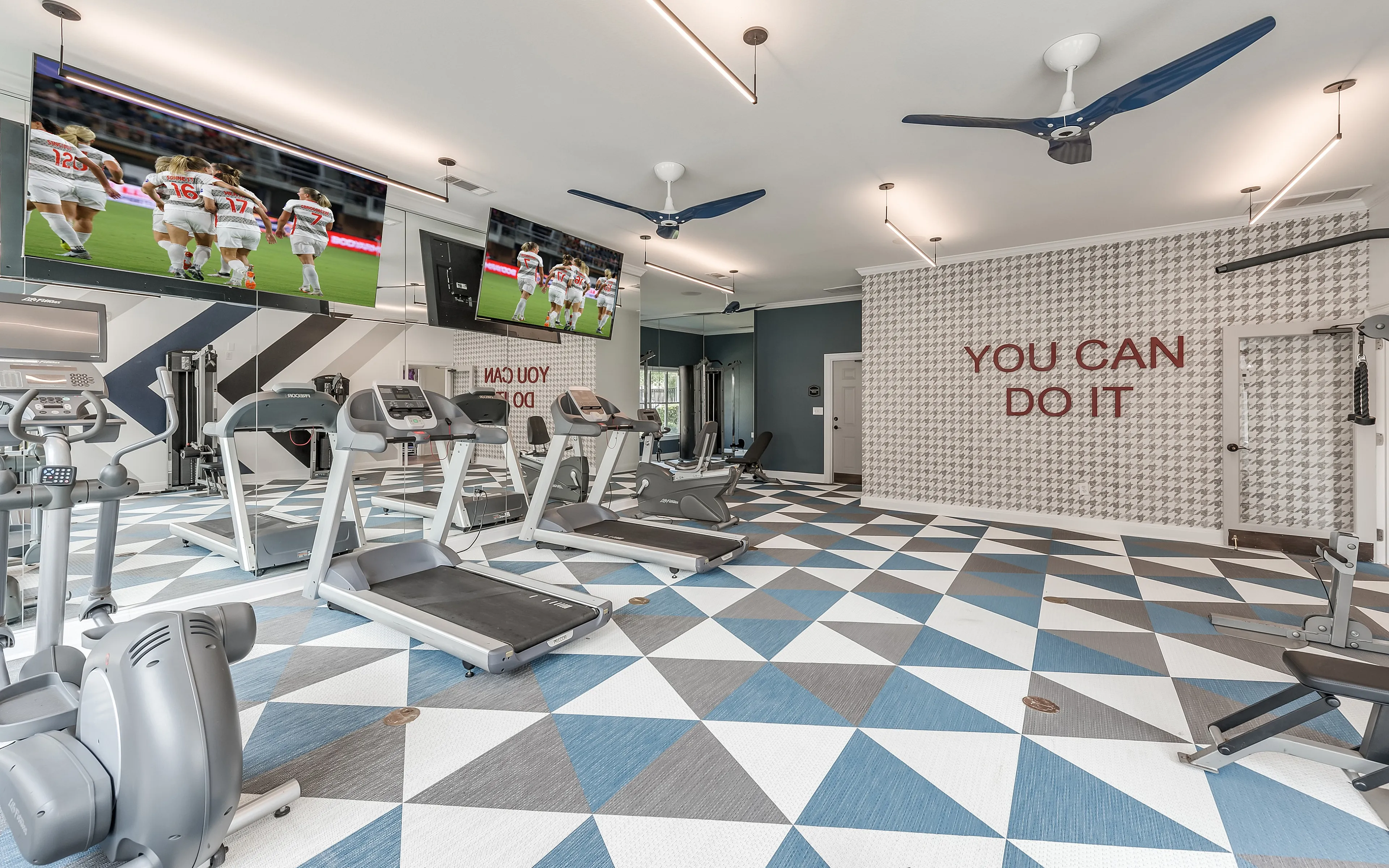 Modern apartment gym with sleek treadmills, vibrant geometric flooring, motivational wall art, and TVs for entertainment.