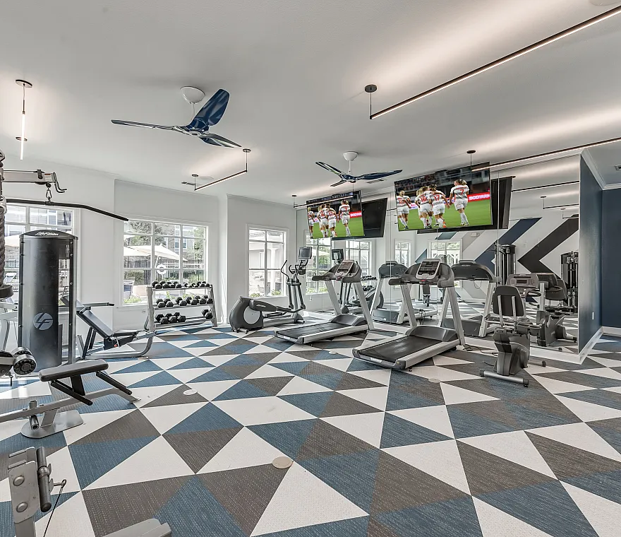 Contemporary and bright fitness center with sleek cardio machines, weight stations, and multiple TVs. Modern geometric flooring adds a stylish touch.