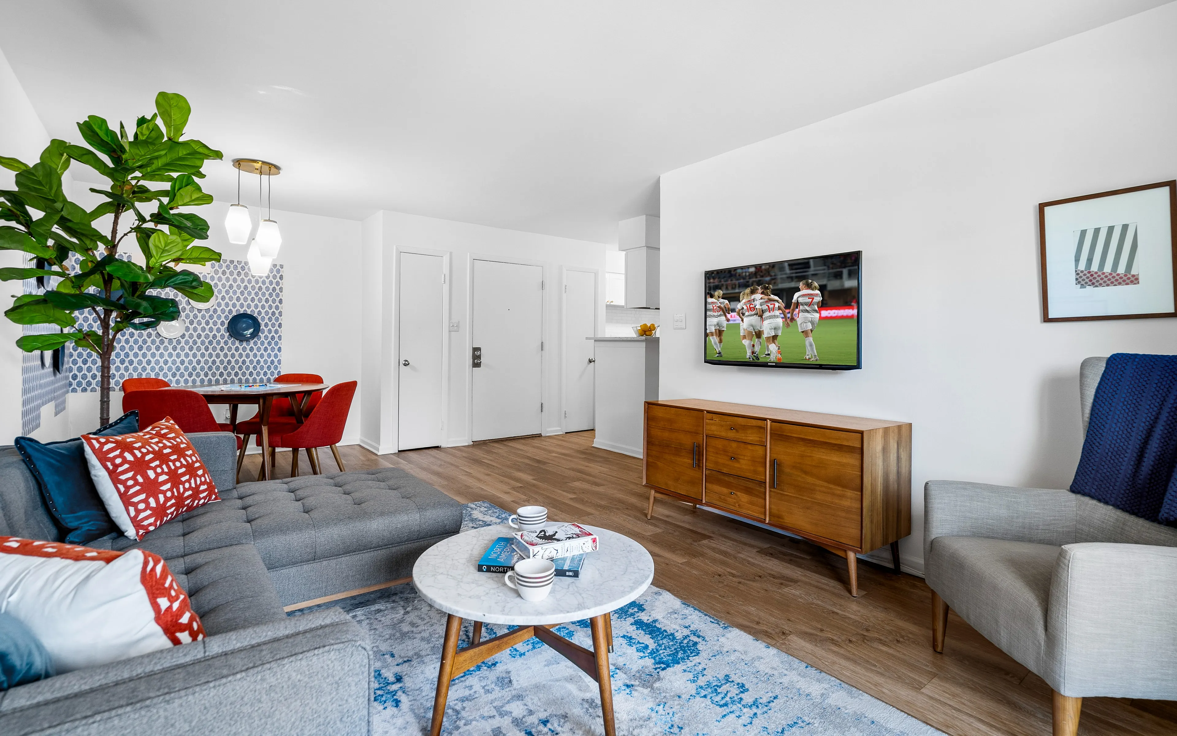 Modern living room with stylish decor, featuring a cozy gray sectional, vibrant red dining chairs, and a sleek entertainment setup.