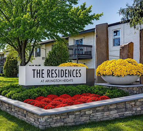 Inviting entrance to The Residences at Arlington Heights, featuring lush landscaping and vibrant flower beds in a serene residential neighborhood.