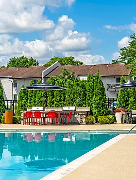 Inviting outdoor pool area with cozy lounge chairs, vibrant umbrellas, and lush green landscaping under a bright blue sky.