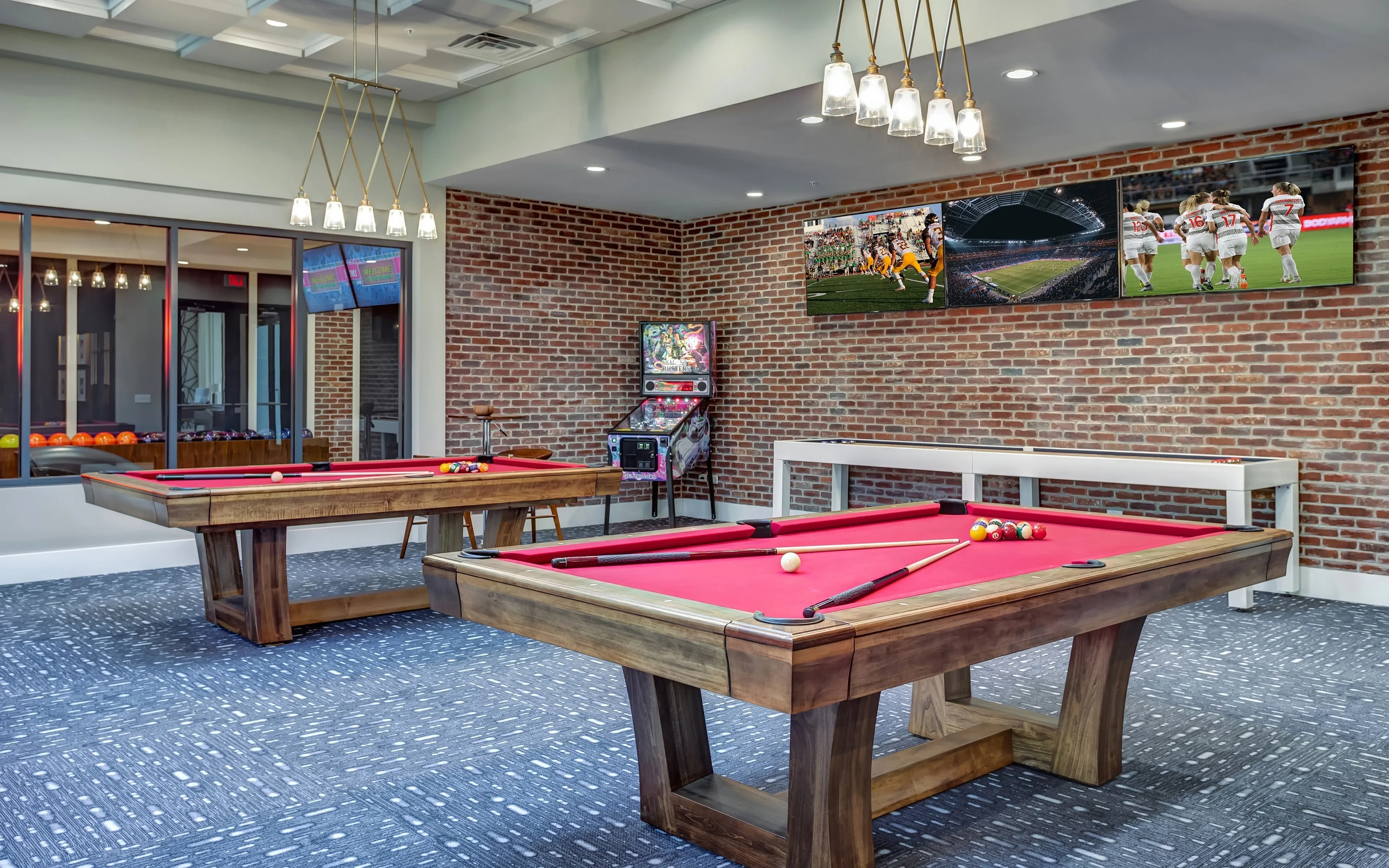 Chic game room with two red felt pool tables, trendy brick walls, and modern fixtures, perfect for entertainment and leisure.