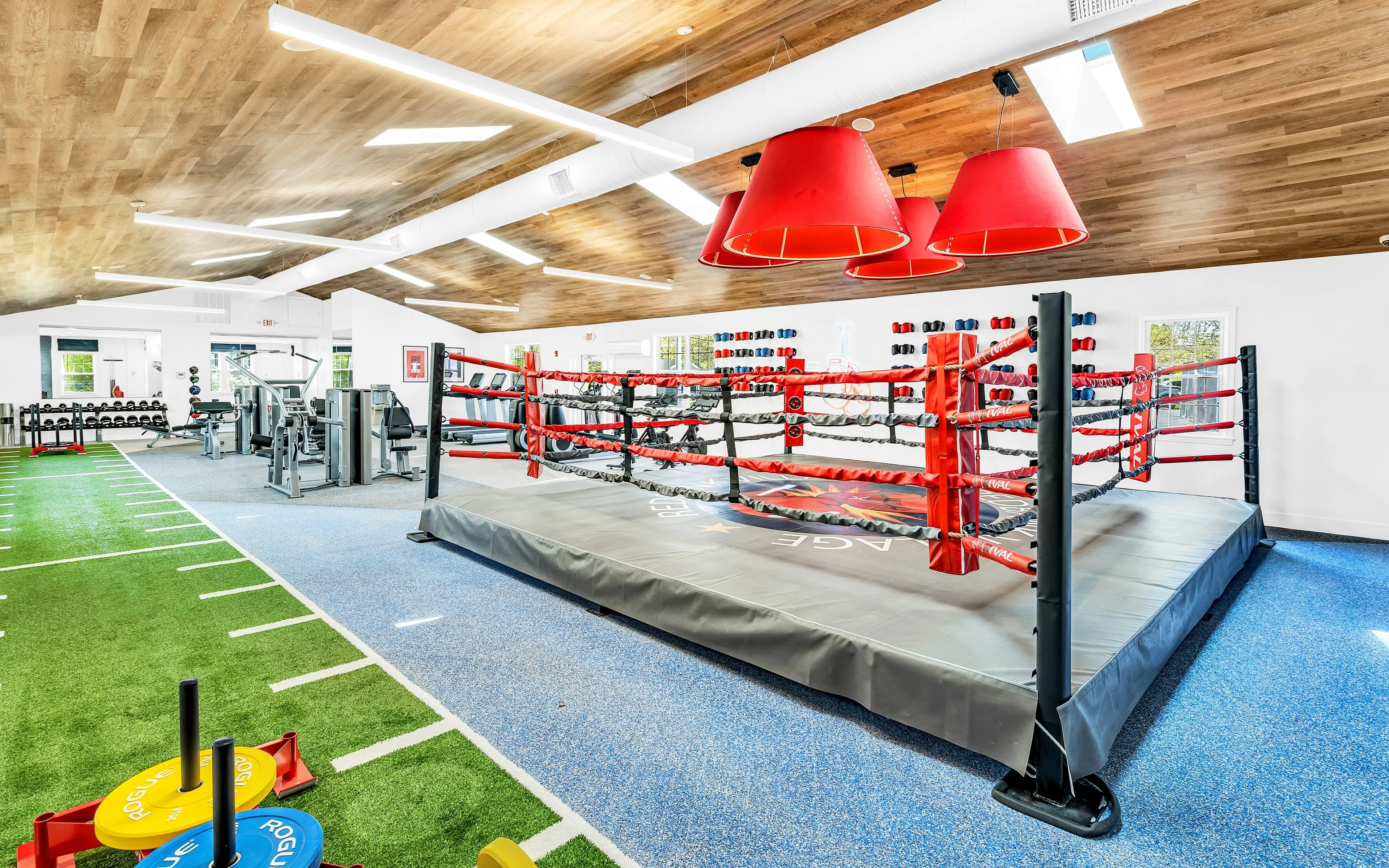 Modern fitness facility featuring a professional boxing ring, state-of-the-art gym equipment, and vibrant red accents for an inspiring workout environment.