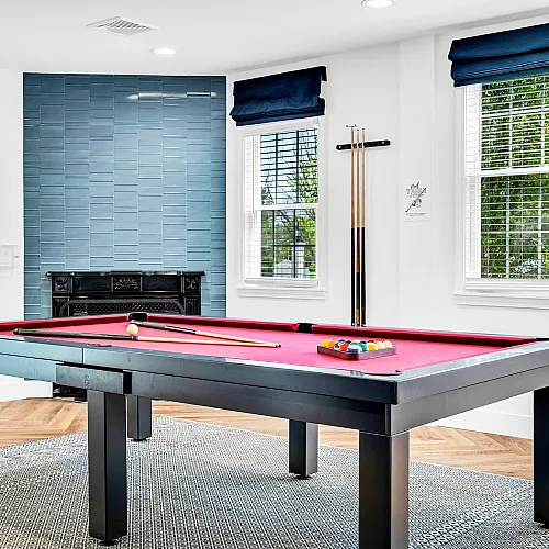 Chic game room featuring a red pool table, stylish blue accent wall, and large windows with natural light, ideal for entertainment.