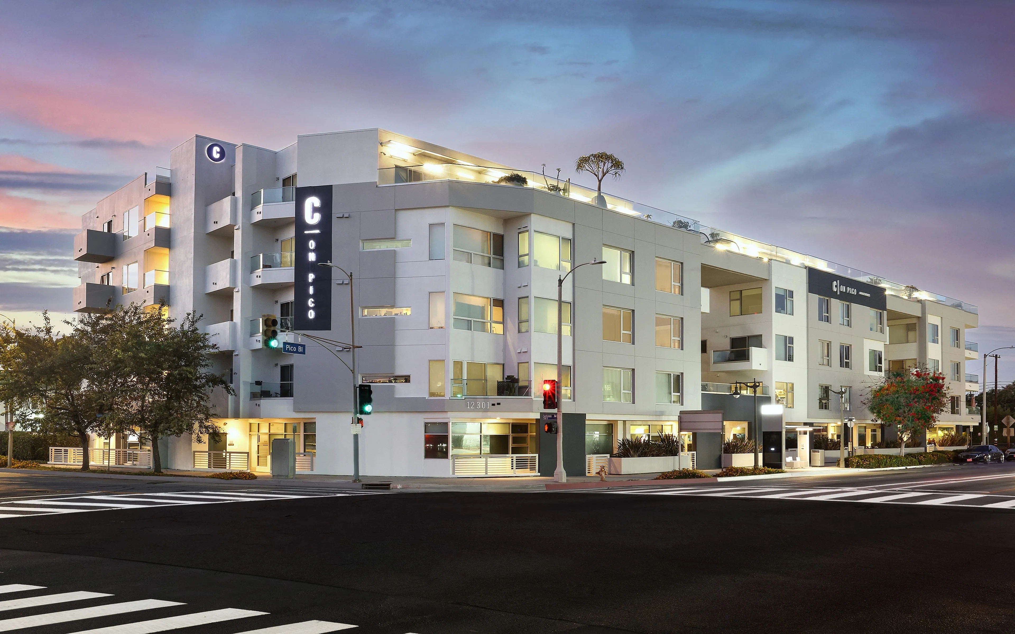 Modern apartment complex at dusk, featuring sleek architecture and warm lighting, set against a vibrant sunset sky, offering urban living with style.