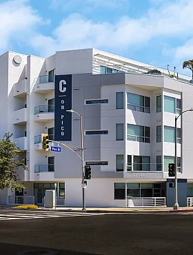 Modern apartment building in sunny urban setting with sleek design, balconies, and tree-lined streets.