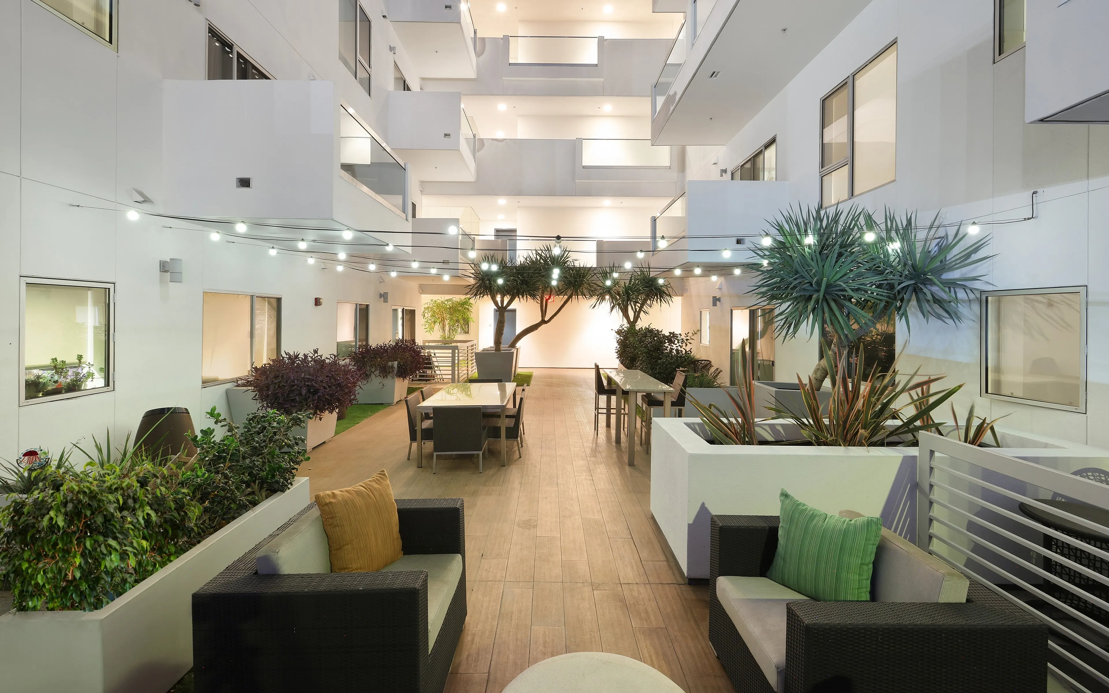 Contemporary apartment complex atrium showcasing elegant outdoor seating, lush greenery, and modern architecture.