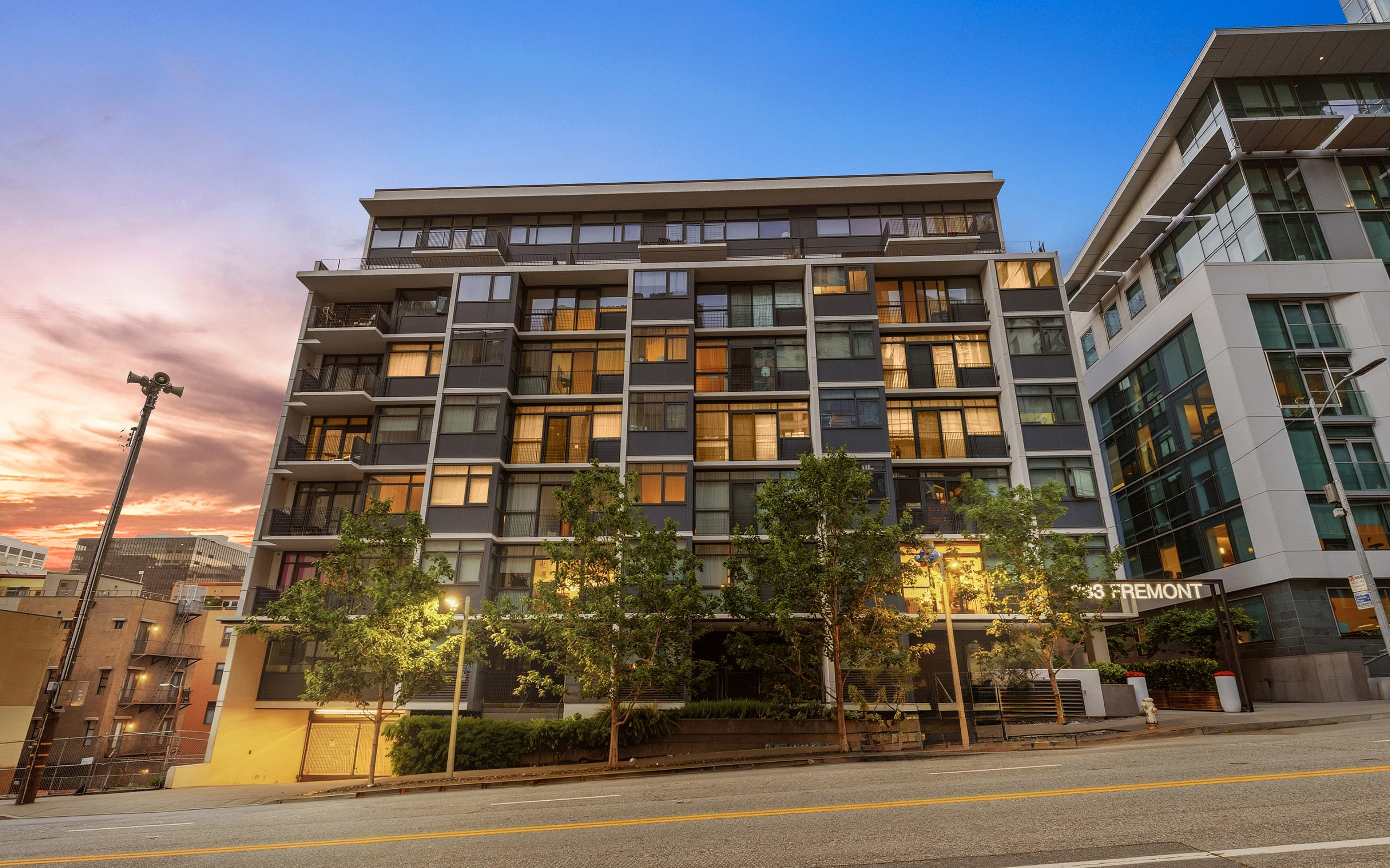 Modern apartment building bathed in a warm sunset glow, showcasing architectural elegance and lush greenery along the facade.
