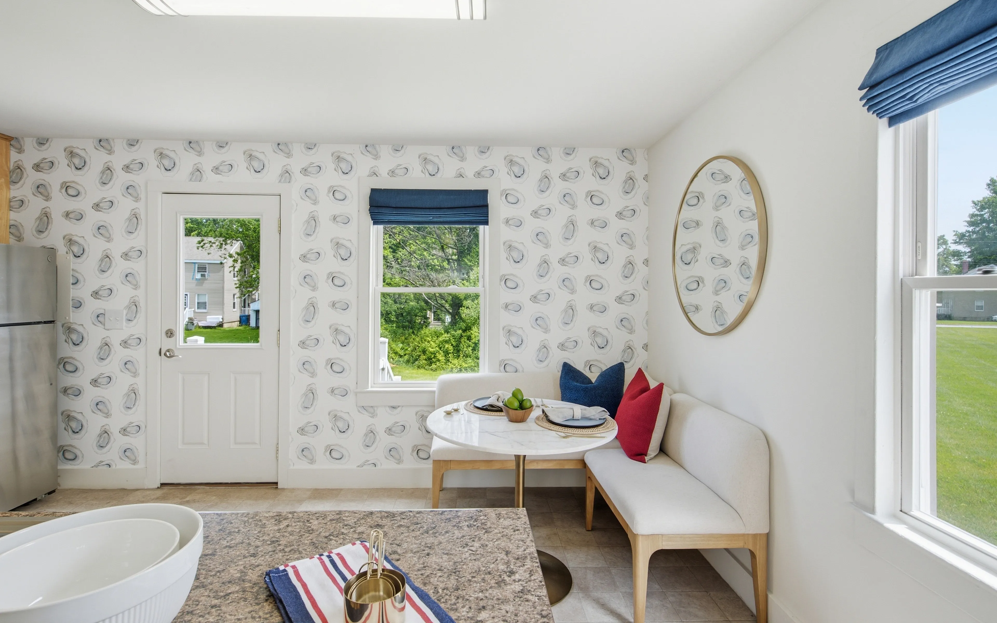 Charming breakfast nook with elegant decor, featuring a modern stainless steel fridge, cozy corner seating with vibrant cushions, and abundant natural light highlighting a scenic garden view.