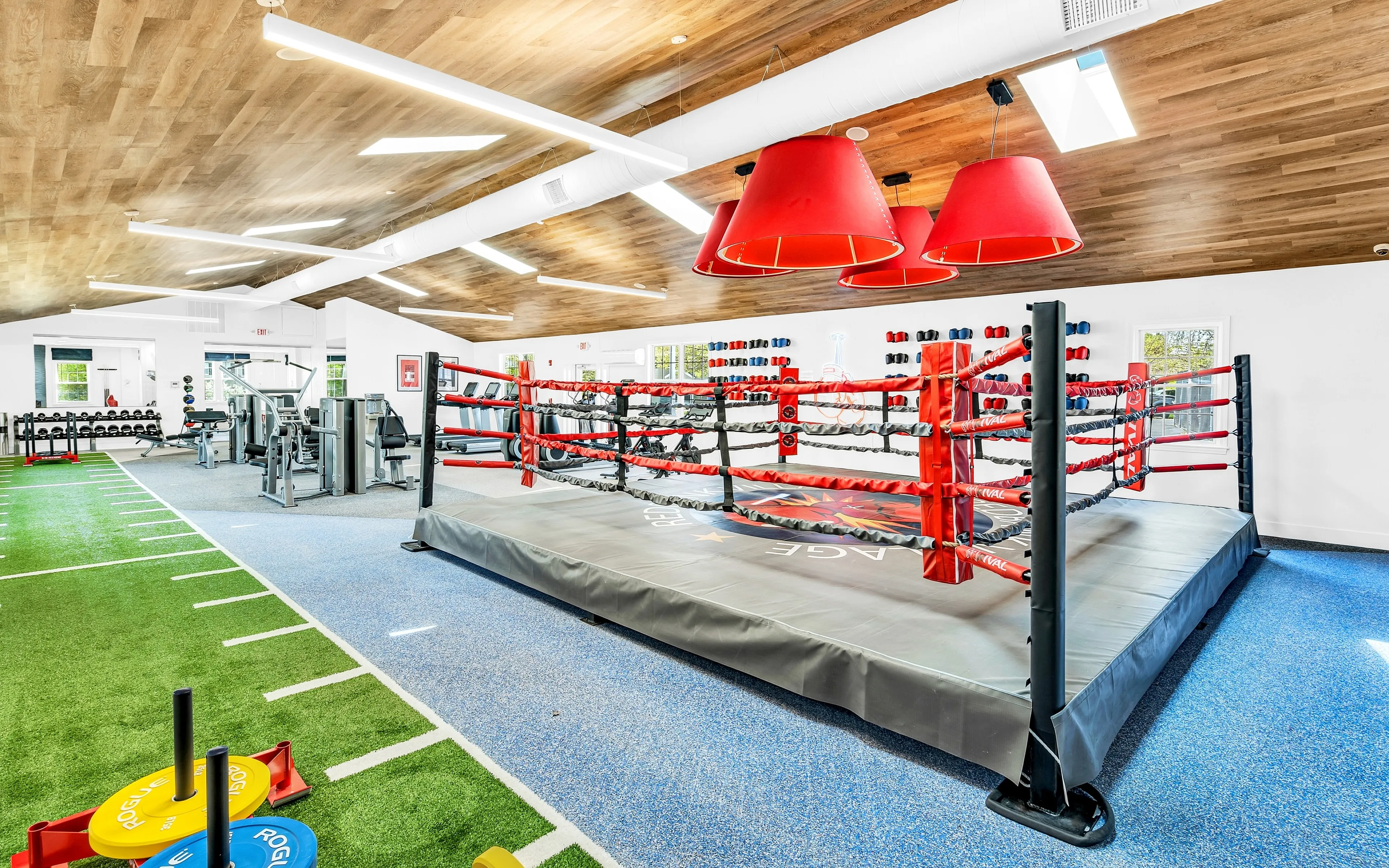 Modern gym interior featuring a vibrant boxing ring, state-of-the-art fitness equipment, and a sleek design with wooden ceilings and dynamic lighting.