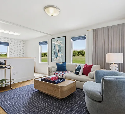 Inviting living room with modern furniture, featuring a cozy sofa and armchair, elegant decor, and natural light from large windows with a scenic view.