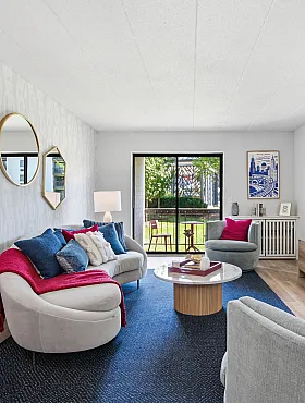 Chic and inviting living room with modern decor, cozy seating, vibrant cushions, and garden view through glass doors.