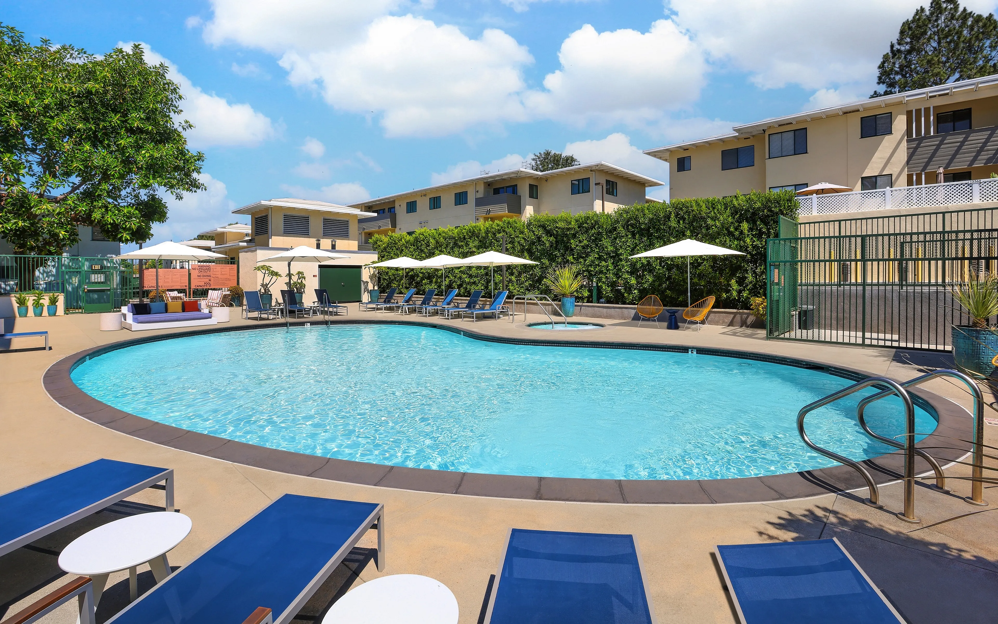 Bright and inviting outdoor pool area with modern lounge chairs, lush greenery, and crisp blue skies.