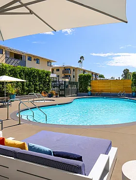 Vibrant pool area with modern lounge chairs and umbrellas, set against a backdrop of lush greenery and stylish apartments.