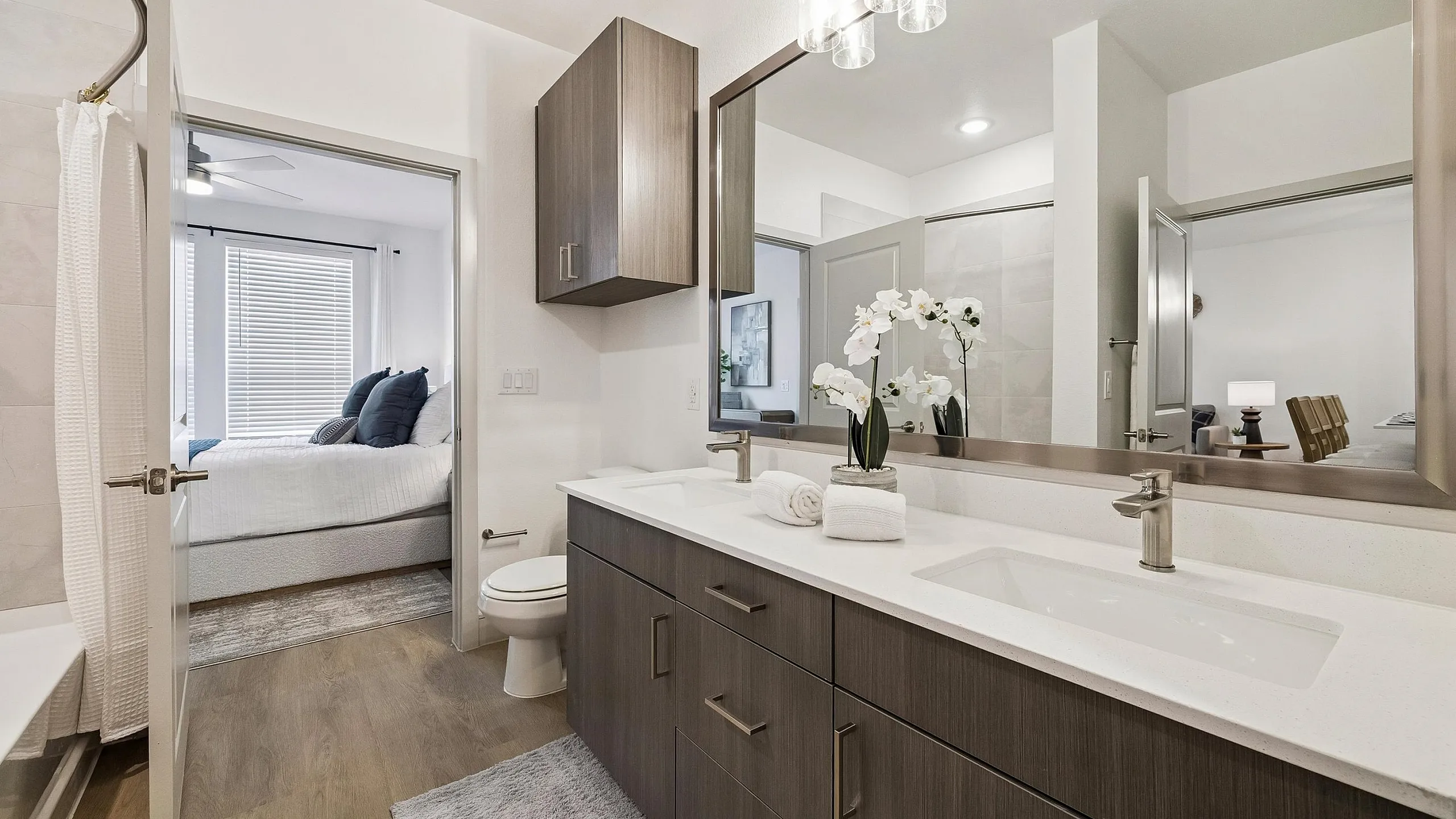 Elegant bathroom with modern fixtures, spacious double vanity, and a view into a cozy, well-lit bedroom featuring sleek furnishings.