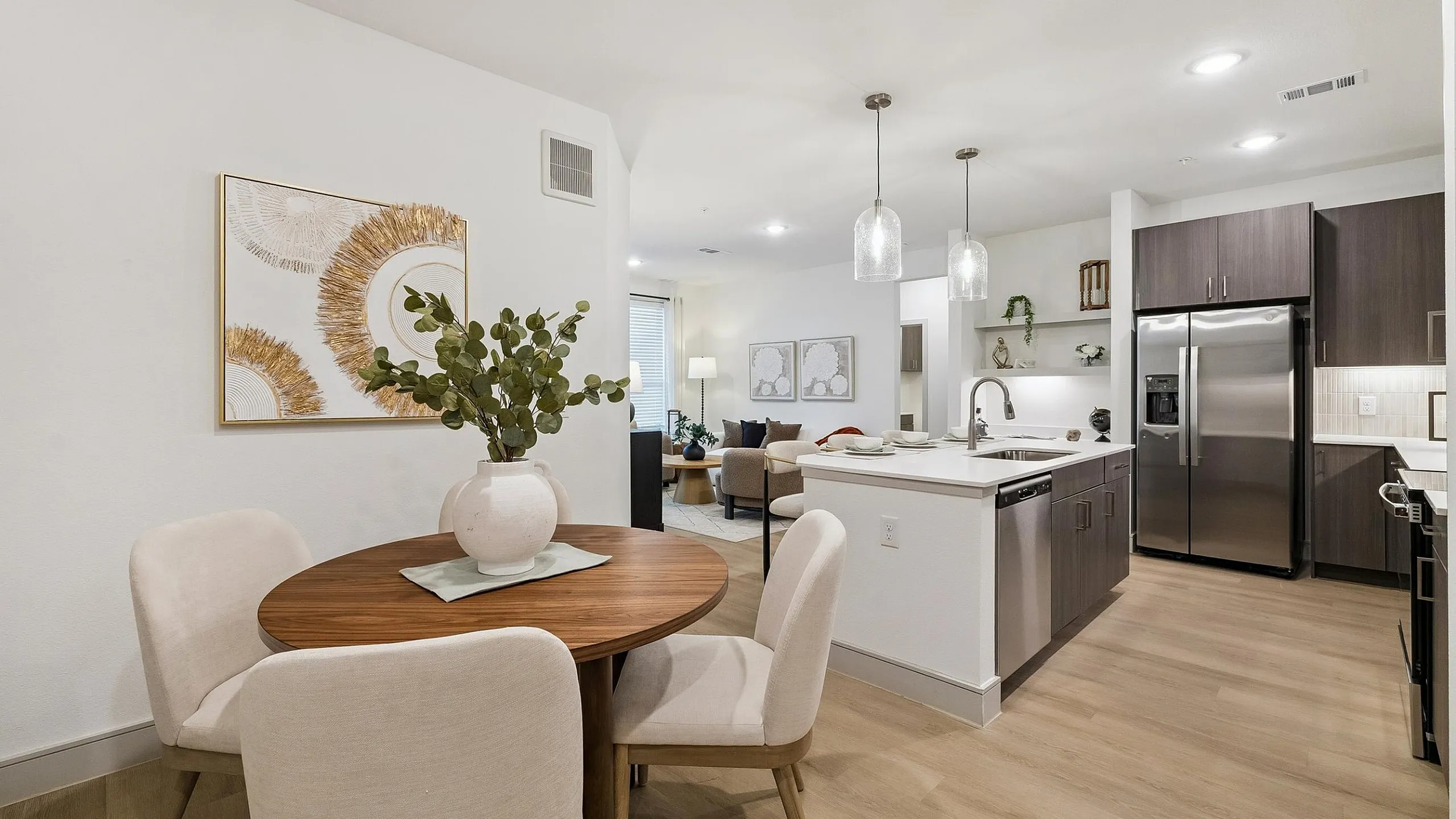 Modern open-concept kitchen and dining area with sleek stainless steel appliances, elegant pendant lighting, and a chic wooden dining table.