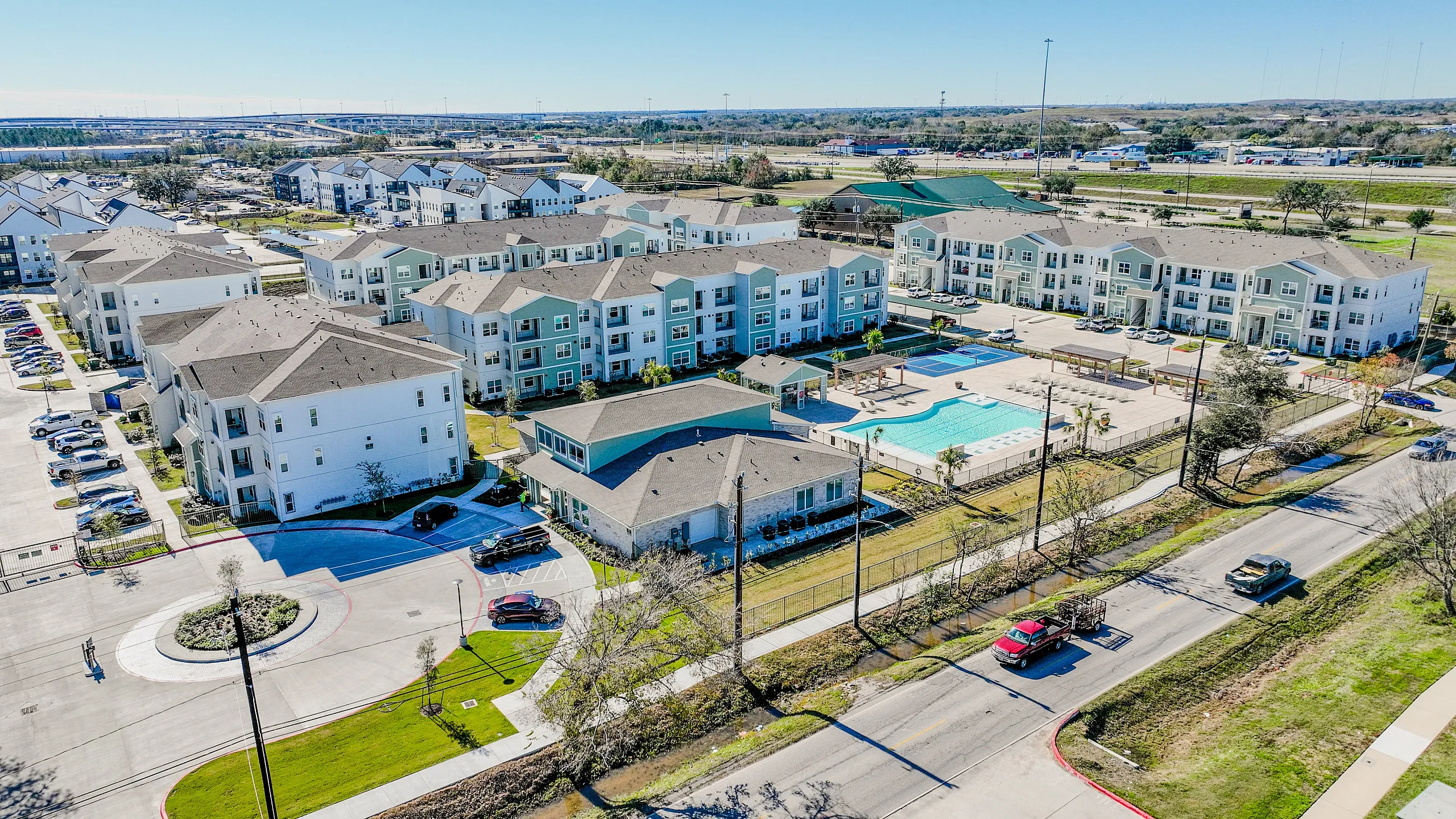 Sprawling modern apartment complex with a sparkling pool, surrounded by lush greenery and ample parking.