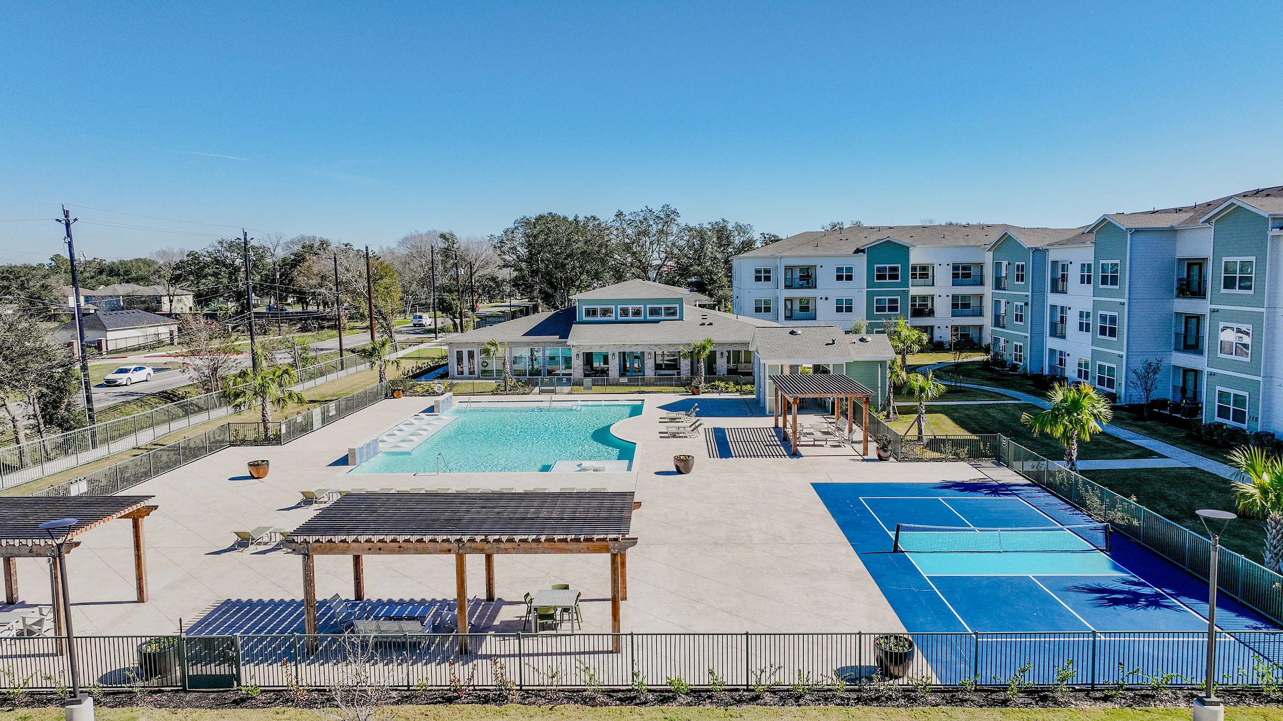 Inviting apartment complex with a resort-style pool, modern building design, and tennis court surrounded by lush greenery.