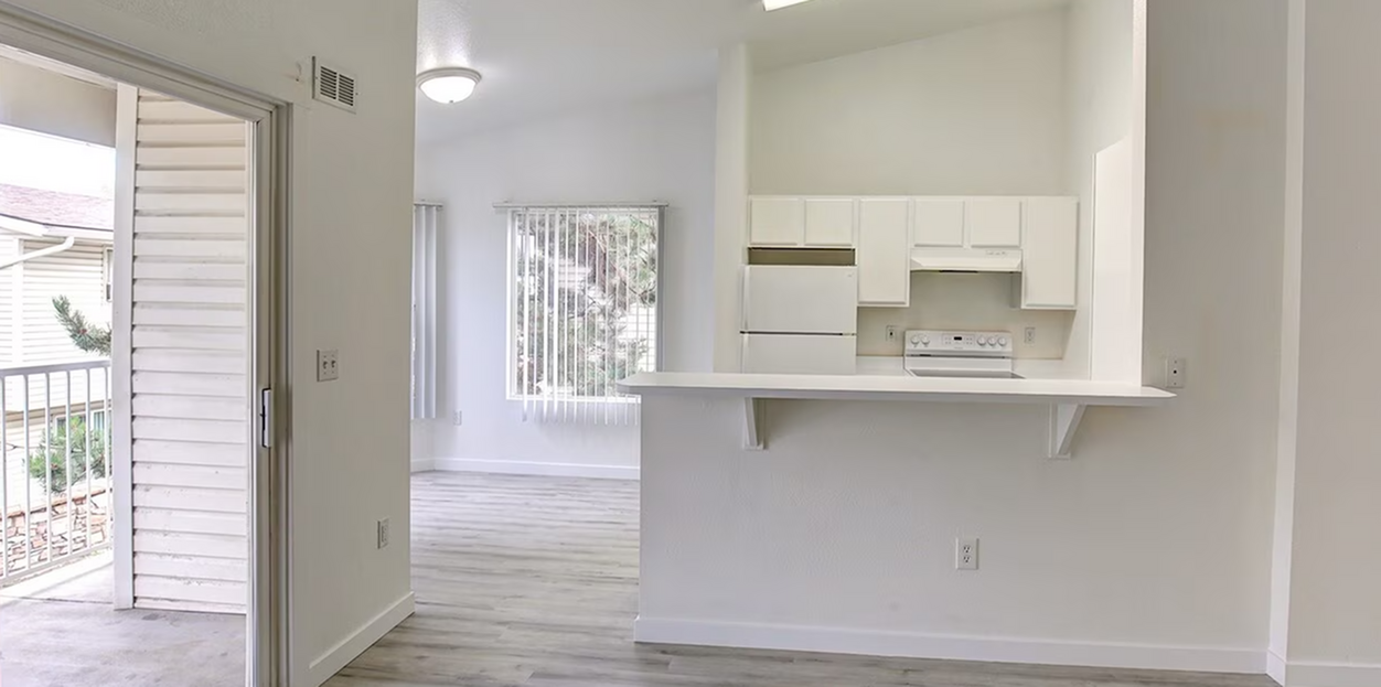 Bright open-concept kitchen with sleek white cabinetry, adjacent to a sunlit living area and balcony access.