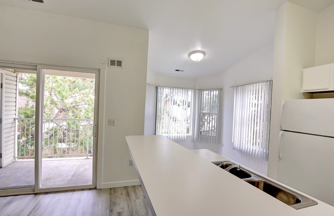 Bright and airy kitchen with an island, large windows, and a view of a private balcony surrounded by greenery.