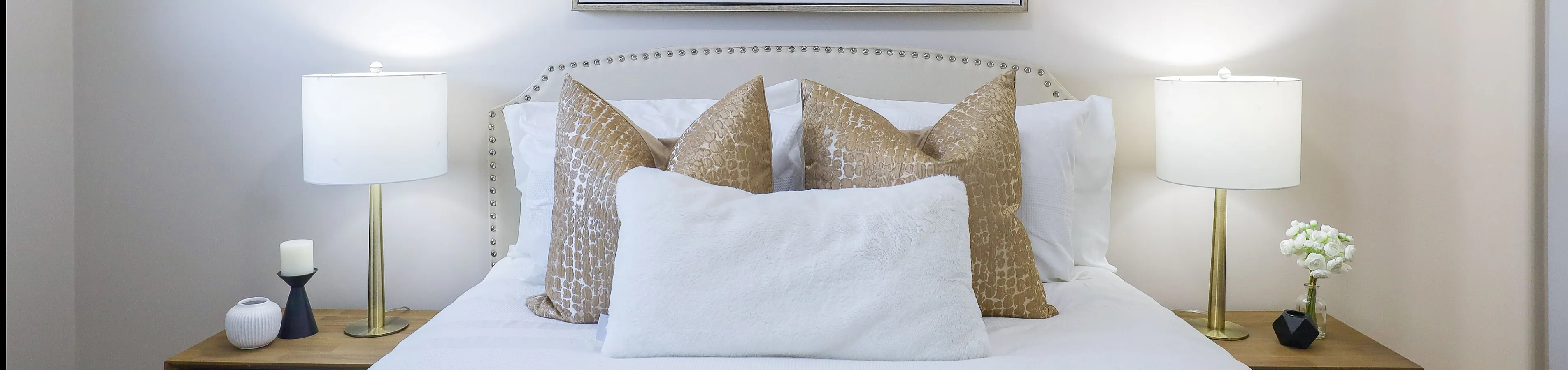 Elegant bedroom with plush bedding, stylish cushions, and modern decor, featuring soft ambient lighting and minimalist artwork.