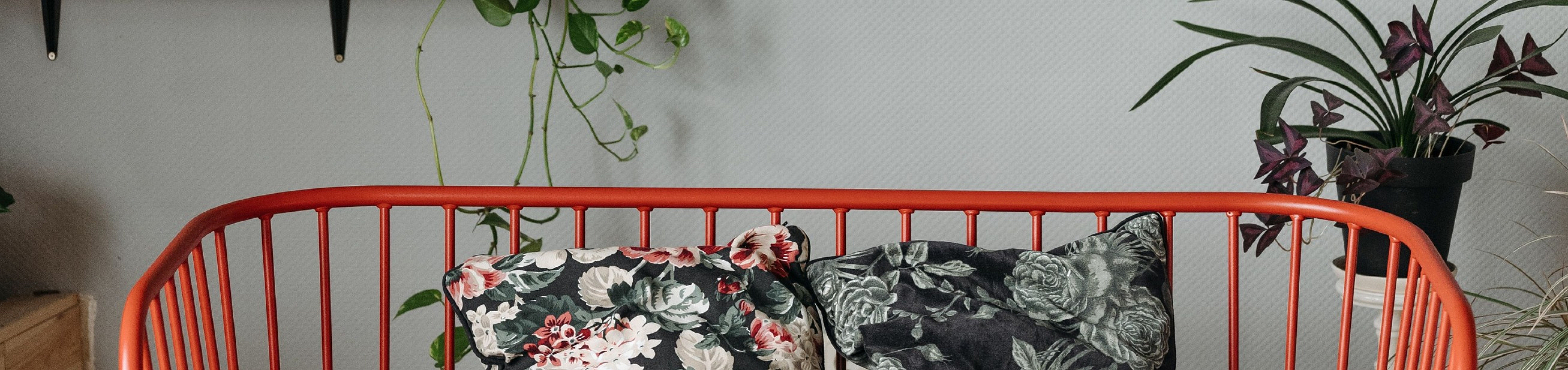 Chic living area featuring a vibrant red sofa with floral cushions, surrounded by lush greenery and elegant wall decor.