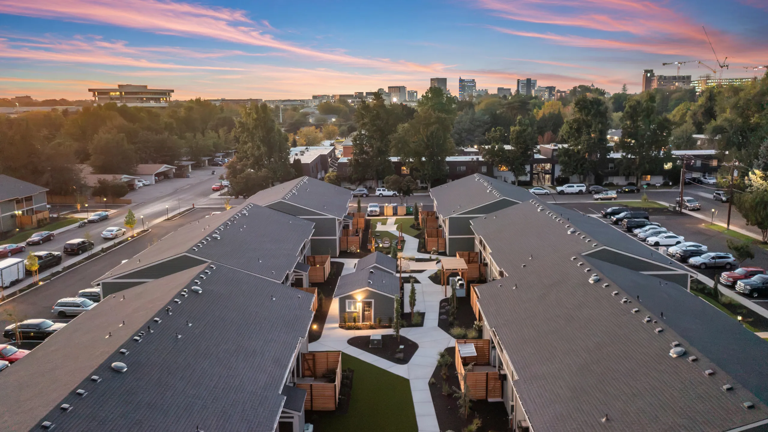 Charming residential community at sunset, showcasing modern townhouses, lush greenery, and city skyline views.