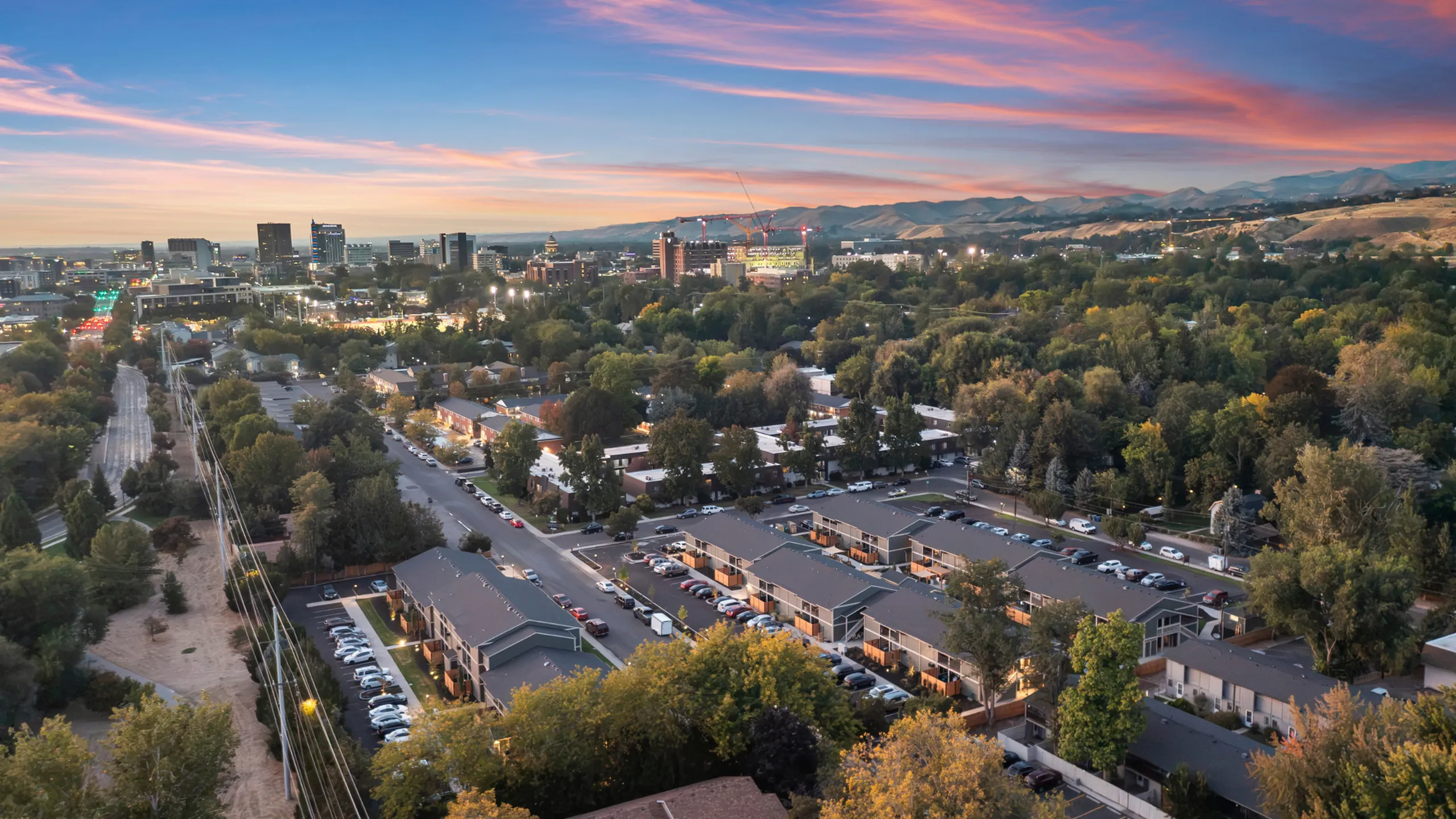 Captivating aerial view of a vibrant cityscape at sunset, showcasing a blend of urban and natural landscapes with modern buildings and lush green spaces.