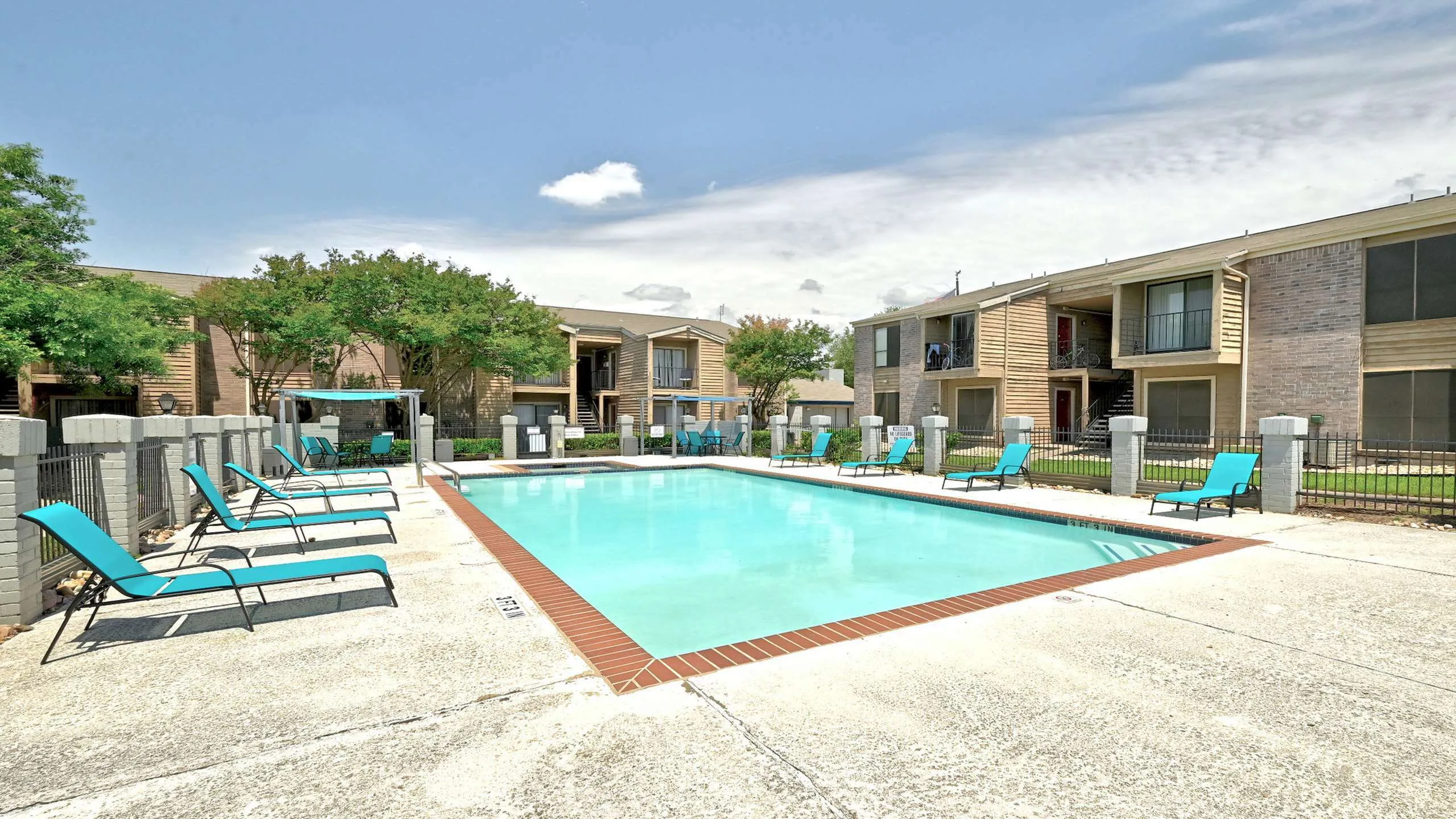Inviting apartment complex with a sparkling pool and cozy poolside seating under a clear blue sky.