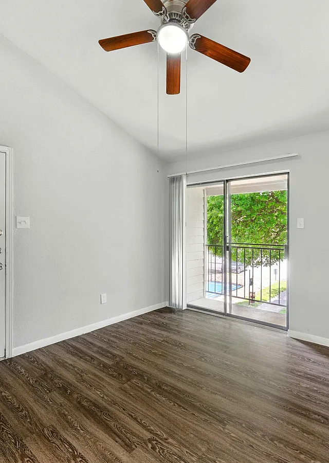 Bright and welcoming room with elegant wooden flooring, a ceiling fan, and a serene view through sliding glass doors, perfect for relaxation.