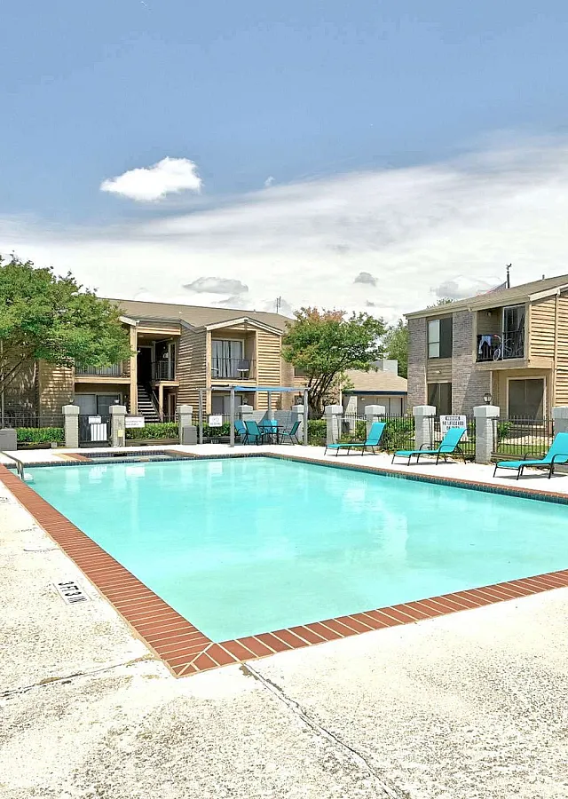 Inviting apartment complex with a sparkling outdoor pool and vibrant sun loungers, surrounded by lush greenery and modern architecture.