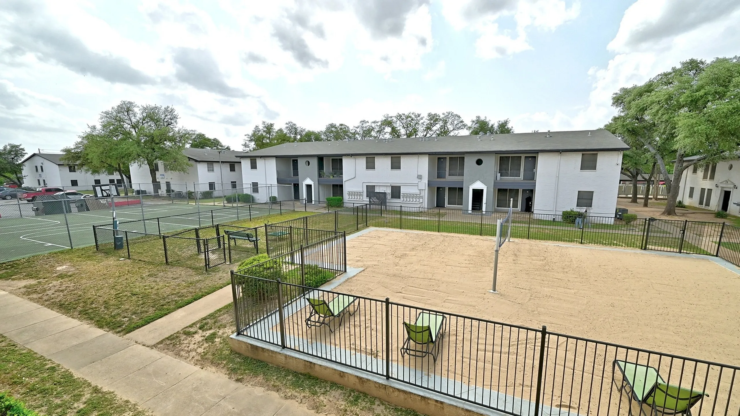 Inviting apartment complex featuring outdoor amenities like a sand volleyball court and tennis courts, surrounded by lush greenery and modern architecture.