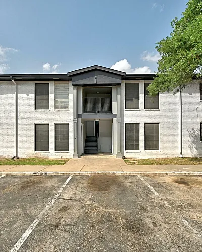 Charming two-story apartment building with modern white brick exterior, ample parking spaces, and lush greenery offering serene living.