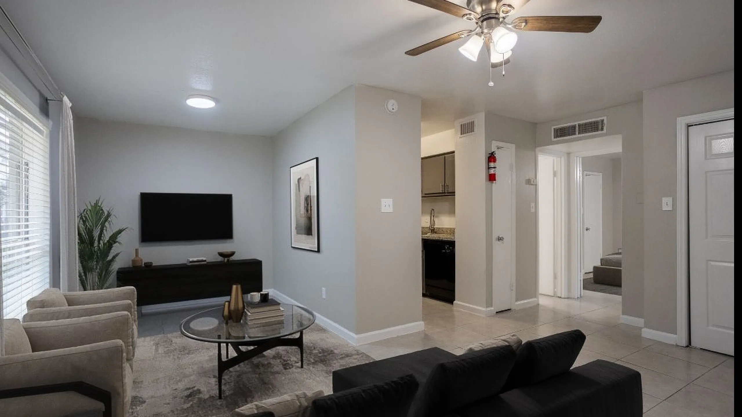Cozy living room with modern decor, ceiling fan, and open access to kitchen and hallway in a bright apartment.