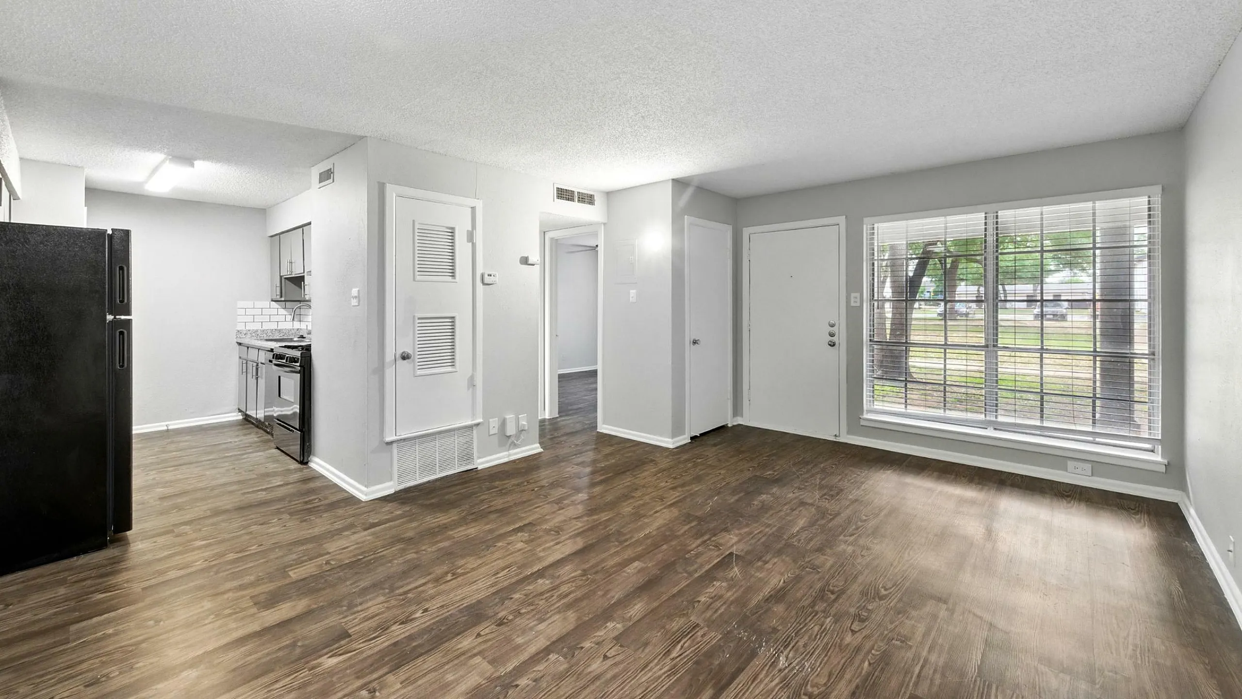Bright apartment with open floor plan, modern kitchen, and large window offering garden views, perfect for stylish living.