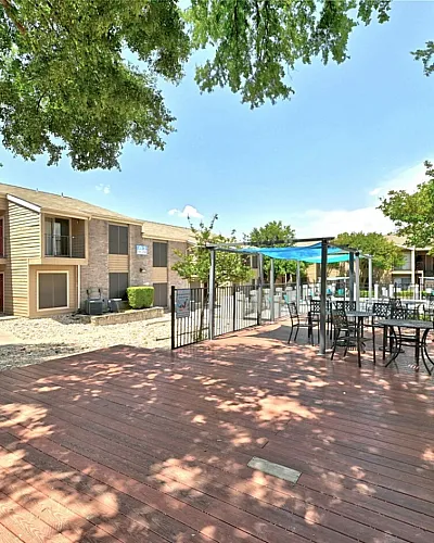 Charming apartment complex with outdoor seating area, shaded by lush trees, and a view of the refreshing pool.