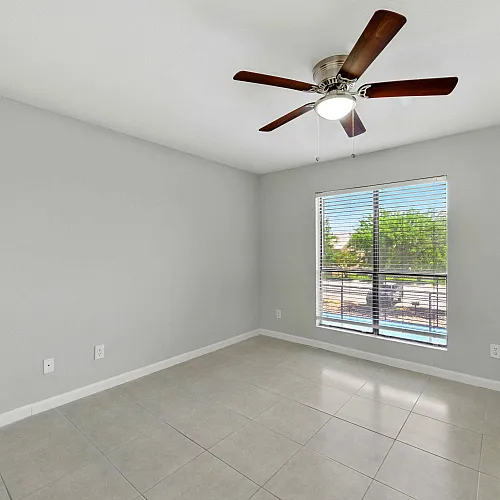 Bright and airy room featuring modern ceiling fan, tile flooring, and large window overlooking lush greenery.