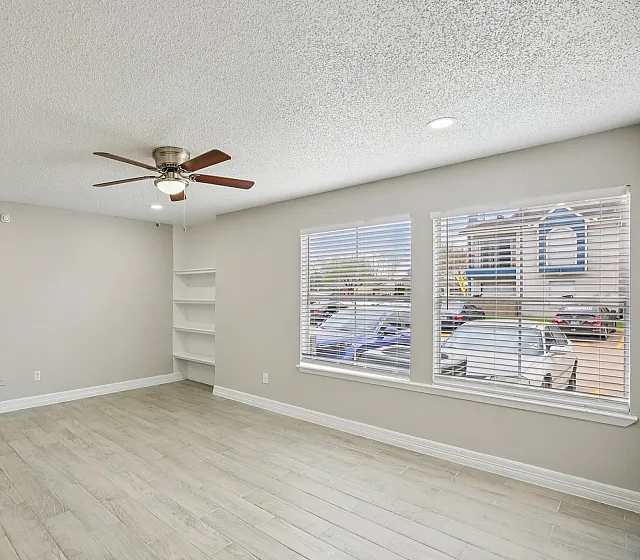 Bright and airy living room featuring elegant wooden flooring, a modern ceiling fan, and large windows with a view of the urban landscape.
