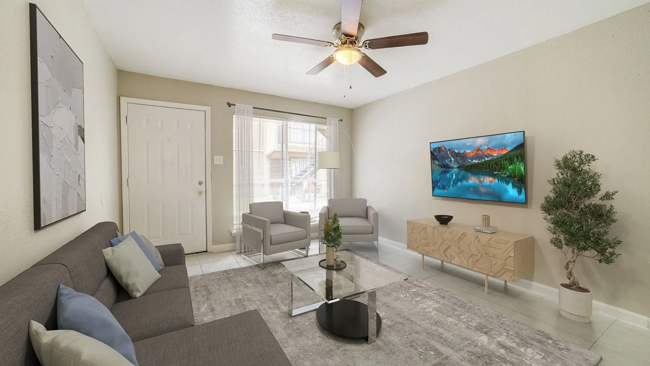 Bright and inviting living room featuring modern gray sofas, sleek glass coffee table, and a mounted TV. Large windows fill the space with natural light, complemented by stylish decor and a ceiling fan for comfort.