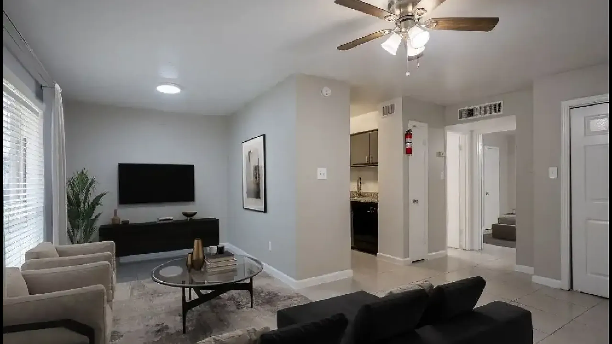 Cozy living room with modern decor, ceiling fan, and open access to kitchen and hallway in a bright apartment.