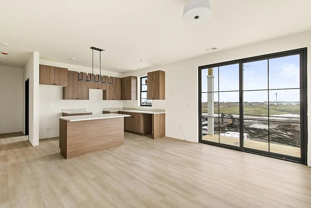 Bright, open-concept kitchen and living area with sleek wooden cabinetry, modern lighting, and expansive windows offering scenic views.